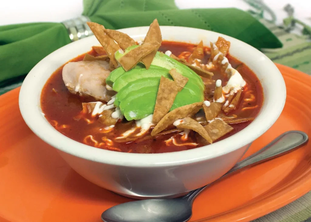 A bowl of tortilla soup with chicken, avocado, and sour cream.