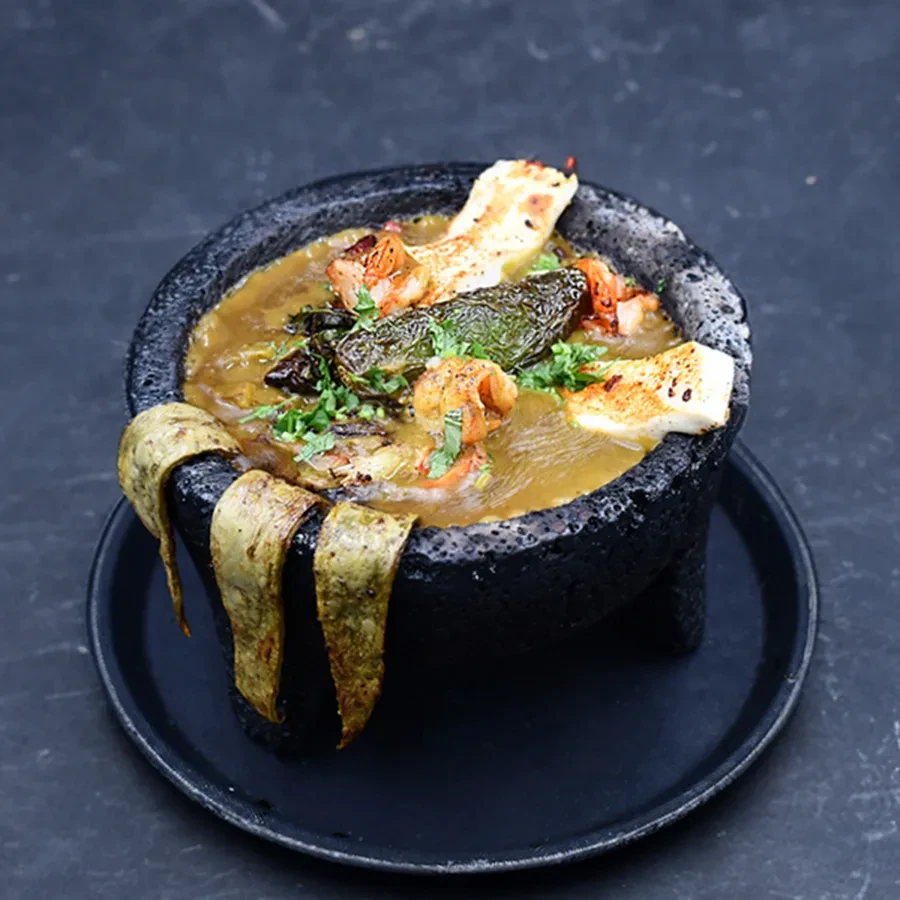 Molcajete bowl with shrimp, melted cheese, and green chile.