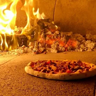 Pizza cooking in a wood-fired oven, with bright flames and embers.