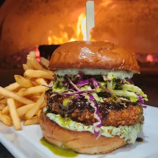 Gourmet burger and french fries on plate with wood-fired oven background.