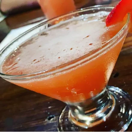 Pinkish-orange frothy cocktail in a martini glass with a strawberry garnish.