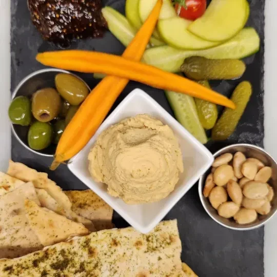 Charcuterie board with hummus, flatbread, olives, nuts, and assorted appetizers.