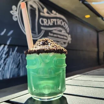 Green tiki cocktail in face glass, dark topping, with "CRAFT ROOTS".