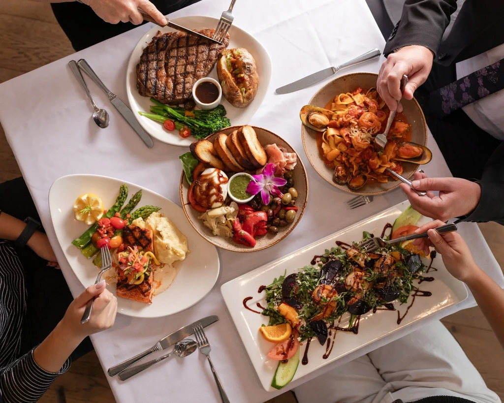 Overhead shot: people dining on gourmet salmon, pasta, charcuterie, and salad.