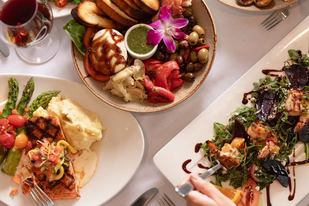 Top-down view: antipasto, salmon, salad, and a hand holding a fork.