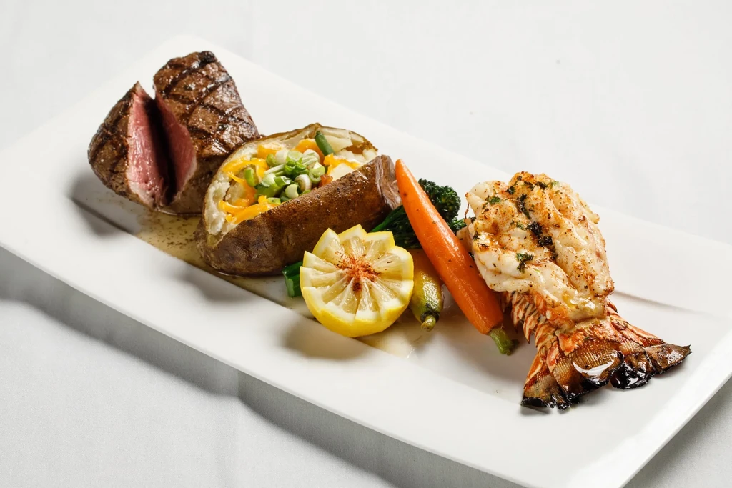 Professionally plated surf and turf with steak, lobster, potato, and vegetables.