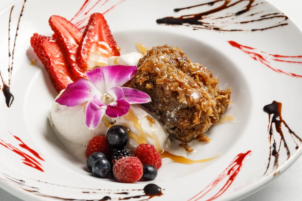 Artfully plated dessert with coconut cake, white ice cream, berries, and orchid.
