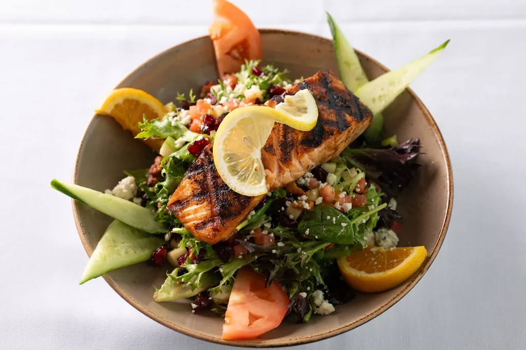Grilled salmon salad with lemon, cheese, nuts in brown rustic bowl.