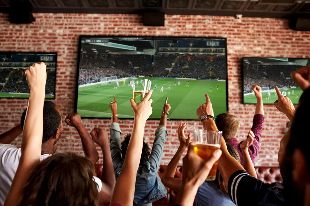 Bar patrons excitedly watching a soccer game on large TV screens.