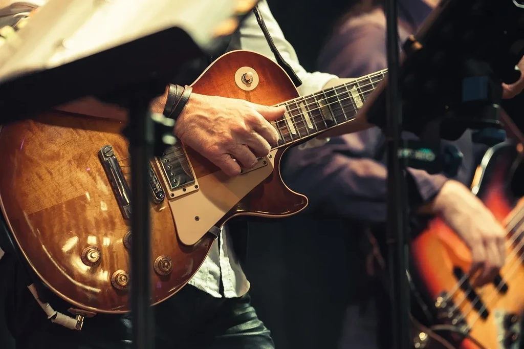 Close-up of hands playing a sunburst electric guitar on a dimly lit stage.