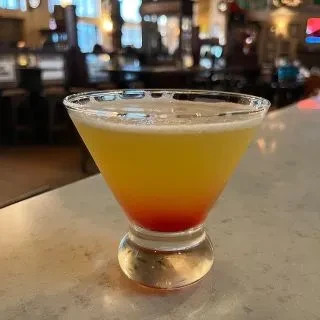Tequila Sunrise-like cocktail in a martini glass at a bar.
