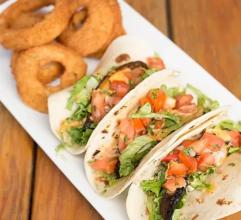 Three soft tacos with lettuce, tomato, sauce and crispy onion rings.