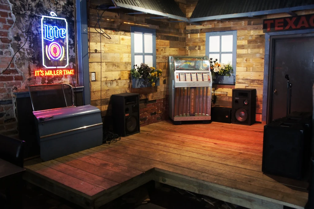 Rustic bar interior with Miller Lite sign, jukebox, and stage.