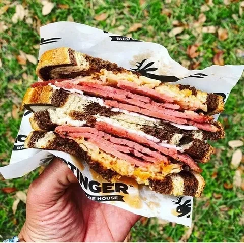 Hand holds a cut, generously filled pastrami sandwich on rye.