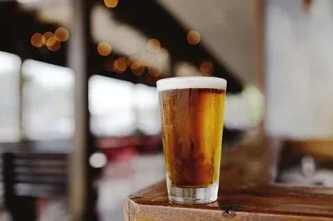 Frosty glass of amber beer with foam on a rustic wooden surface.