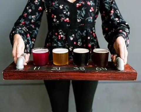 Person holding a wooden beer flight with four numbered, cold beers.