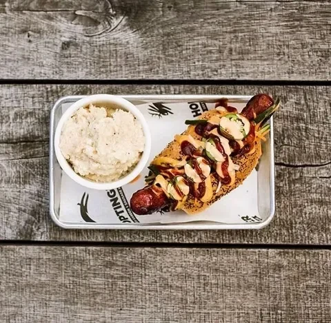 Gourmet sausage with jalapeños, sauces, and creamy side on tray.