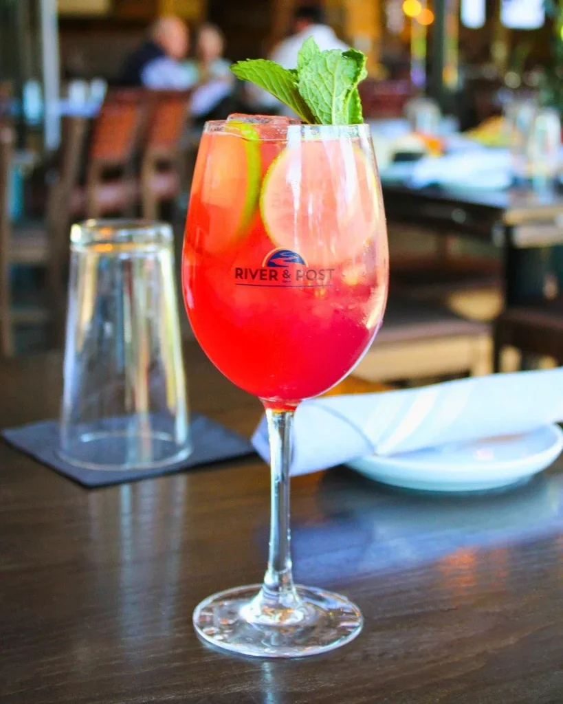 Red cocktail in "RIVER & POST" wine glass with mint and lime.