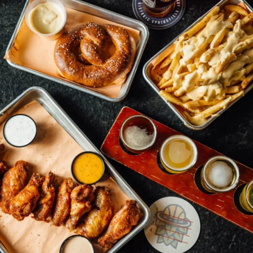 Flat lay of pretzel, loaded fries, chicken wings, and beer flight.
