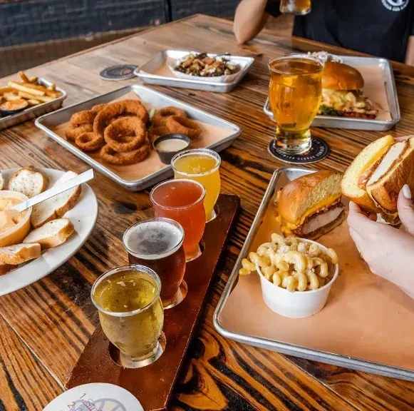 Rustic table with a beer flight, burgers, fries, and onion rings.