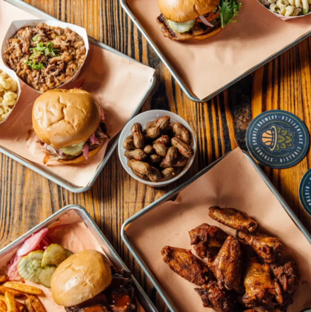 Top-down view: Rustic table with BBQ feast and Sports Brewery coaster.