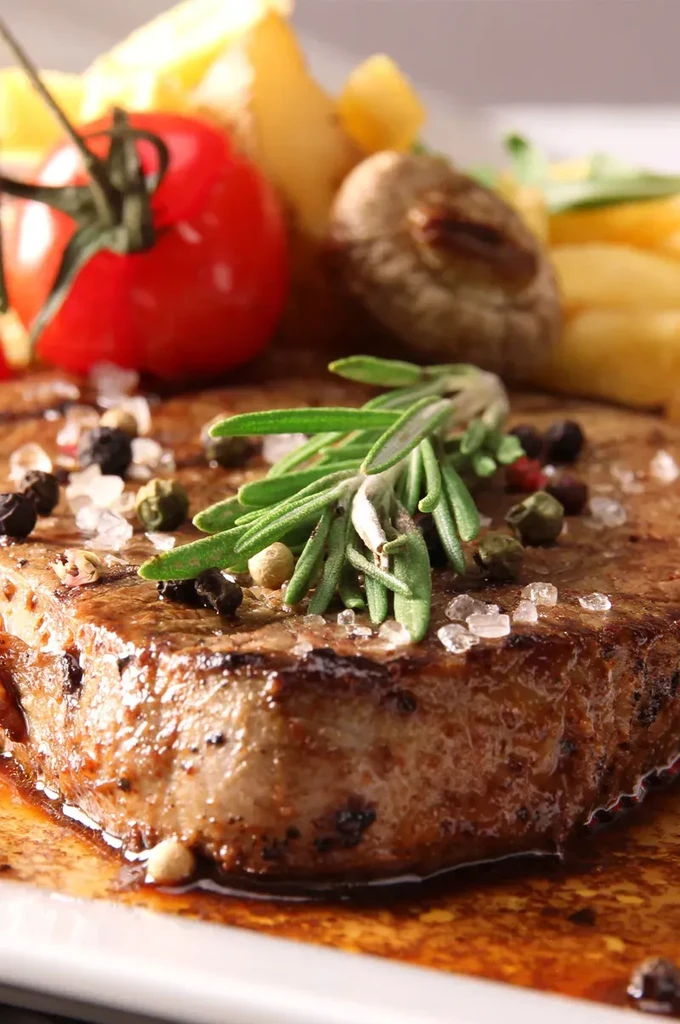 Seared grilled steak on a plate with rosemary, peppercorns, and sauce.