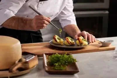Chef's hands meticulously garnish three seafood dishes with tweezers.