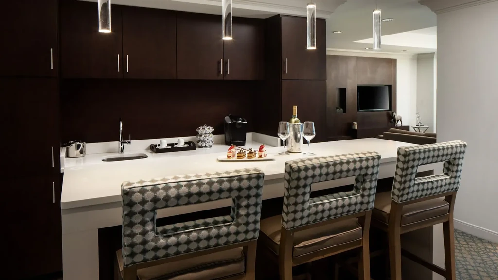 Kitchenette bar with white counter, stools, coffee maker, wine, desserts.