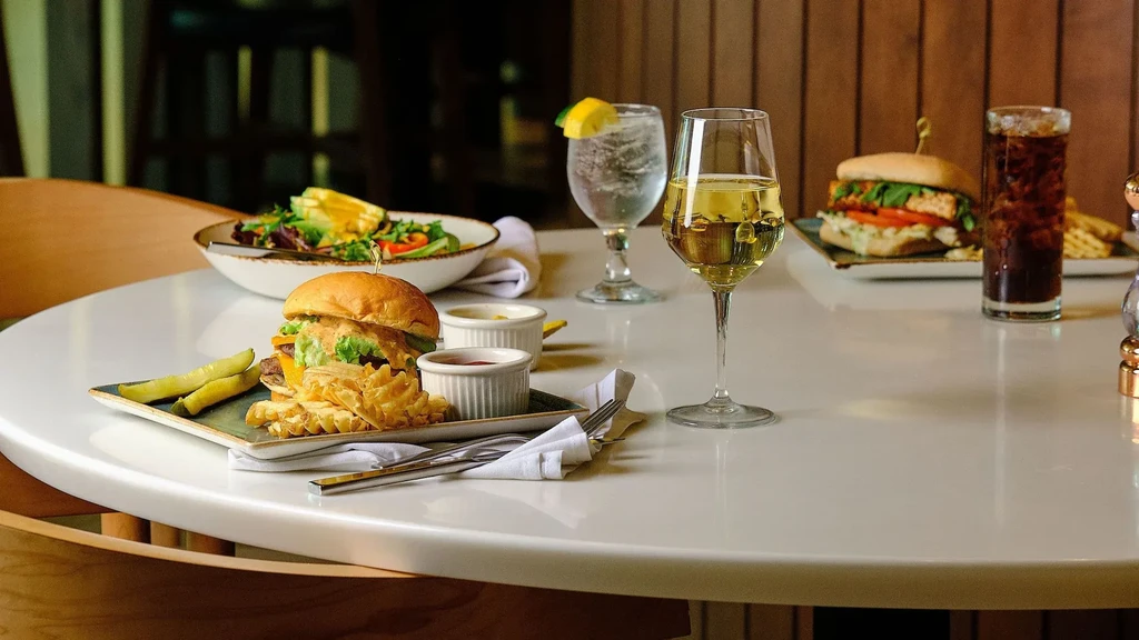 Restaurant table full of burgers, fries, salad, wine, and soda.