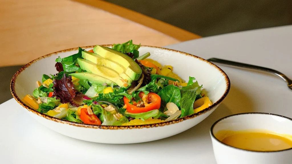 Fresh salad in a white bowl with avocado, peppers, and dressing.