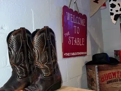 Cowboy boots, 'WELCOME TO THE STABLE' sign, Budweiser crate, and hat.