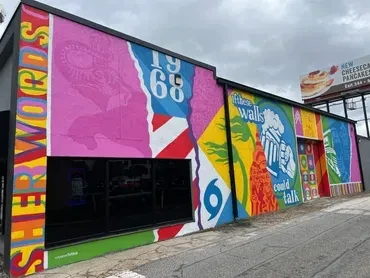 One-story building with a vibrant mosaic mural, including '1968' and 'SHERWOODS'.