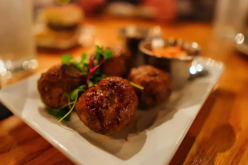 Close-up of four browned appetizers with green garnish and orange dip.