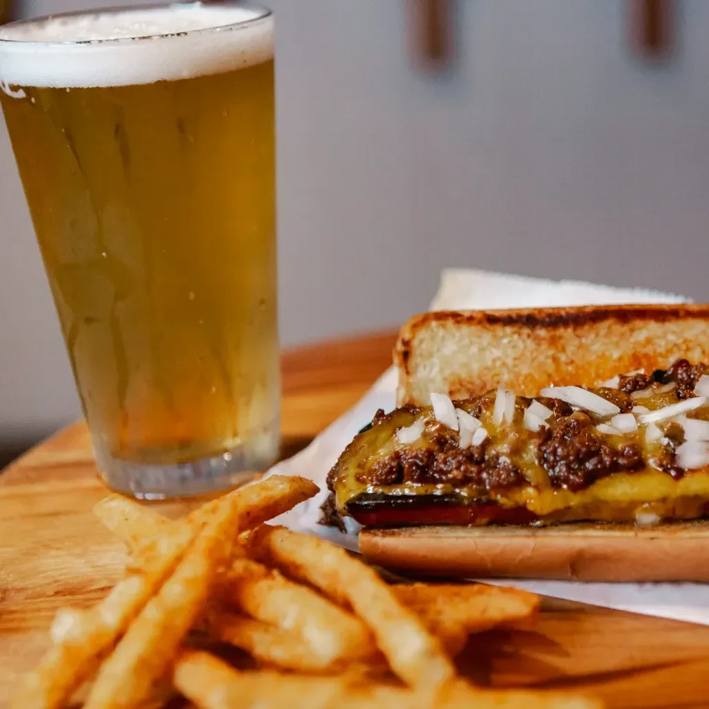 Chili cheese hot dog, french fries, and beer on a wooden table.