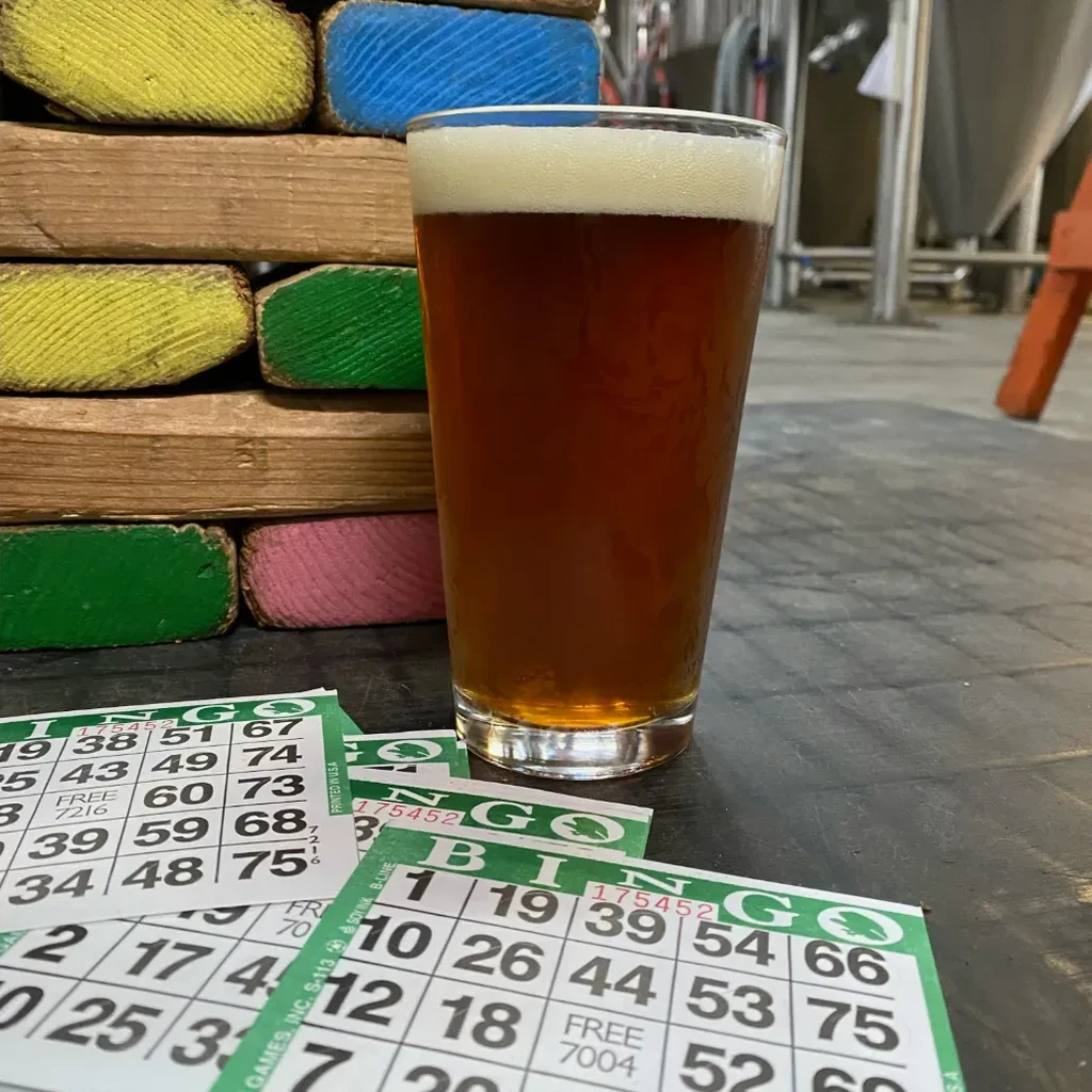 Pint glass of beer, colorful blocks, bingo cards, brewery background.