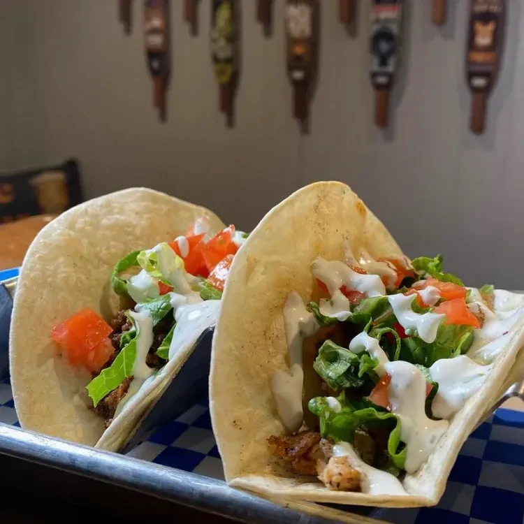 Two soft-shell tacos on tray with meat, lettuce, tomatoes, sauce.