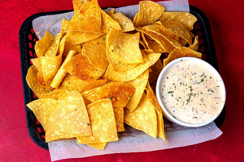 Black basket of seasoned chips and creamy dip on red.