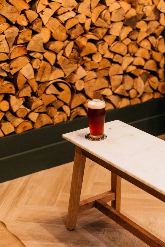 Pint of dark beer on marble table against a stacked log wall.
