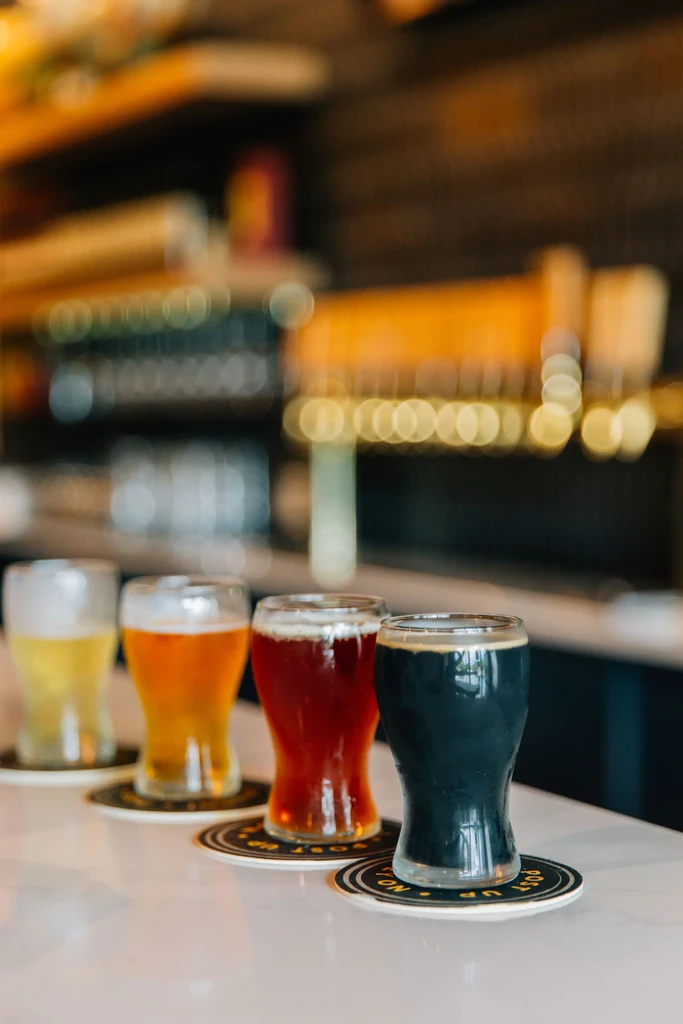 Flight of four beers, from pale yellow to dark, on a bar.