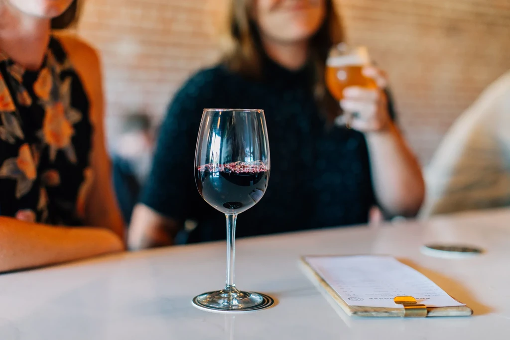 Close-up of red wine glass with blurred people in a bar.