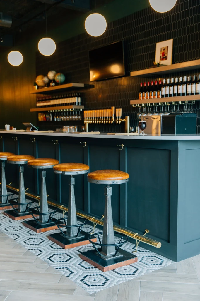Modern bar with teal counter, five industrial stools, beer taps, mosaic floor.