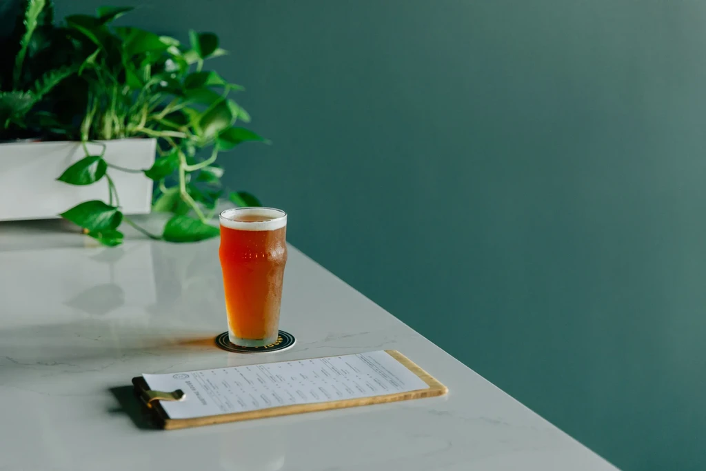 Condensation-covered beer glass, menu on clipboard, plant on stone table.