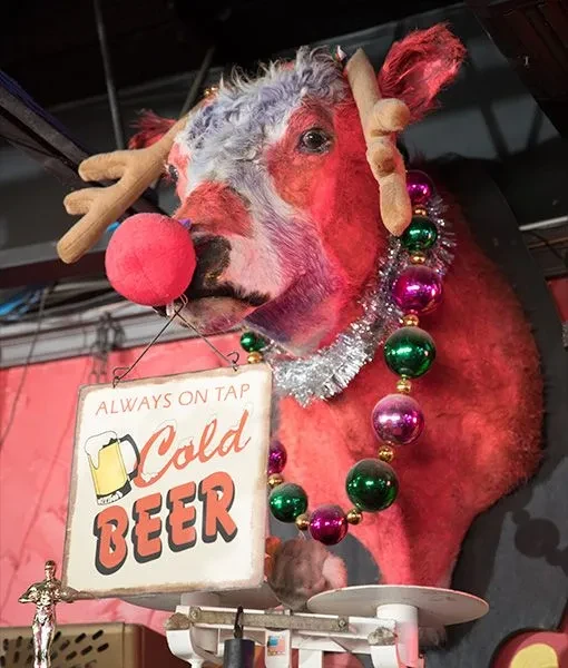 Decorated taxidermied red calf head with antlers, Rudolph nose, and beer sign.