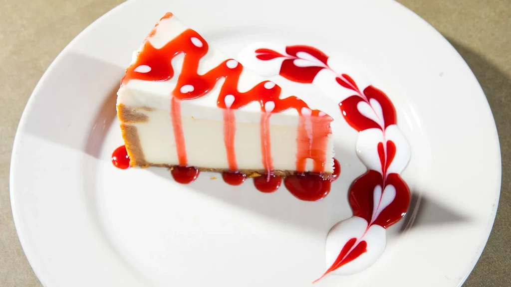 Cheesecake slice with red sauce drizzle and heart shapes on a plate.
