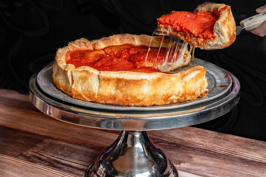 Hand lifts a deep-dish pizza slice, showing long melted cheese strands.