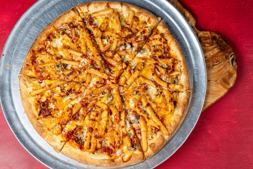 Pizza topped with cheese, meat, and french fries, cut into slices.