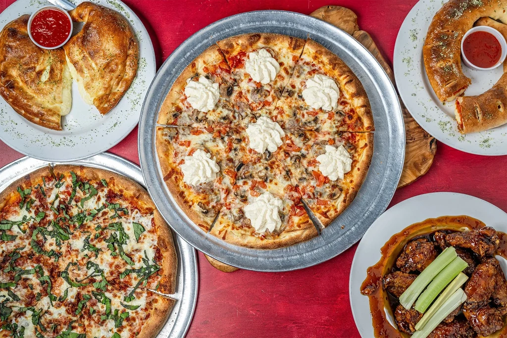 Overhead view of an assortment of Italian-American pizza, calzones, and wings.