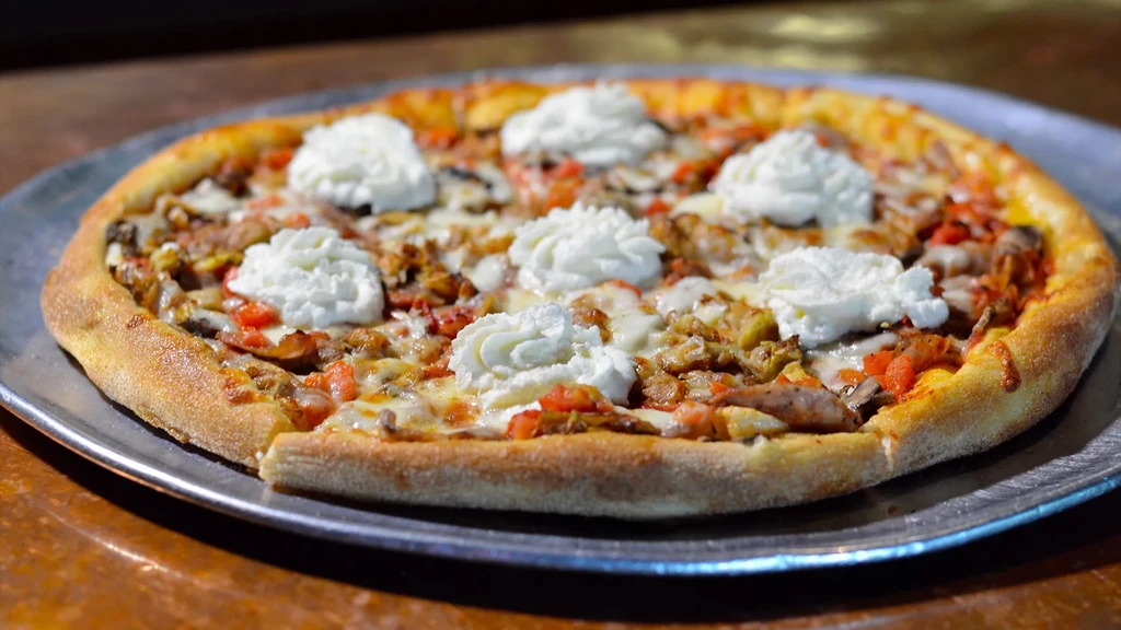 Whole pizza with melted cheese, red toppings, meat, and ricotta dollops.