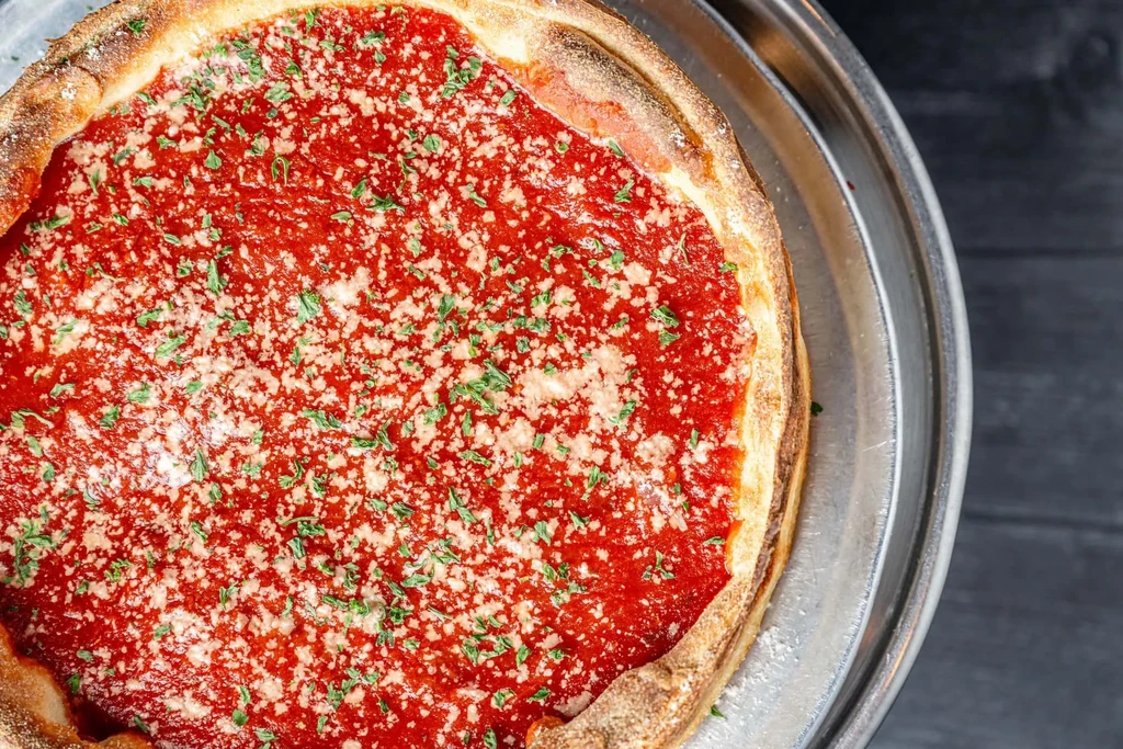 Deep-dish pizza with thick golden crust, red sauce, cheese, herbs.