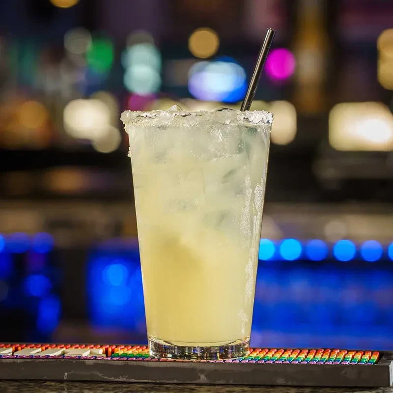 Salt-rimmed cocktail with ice and straw on a colorful bar mat.